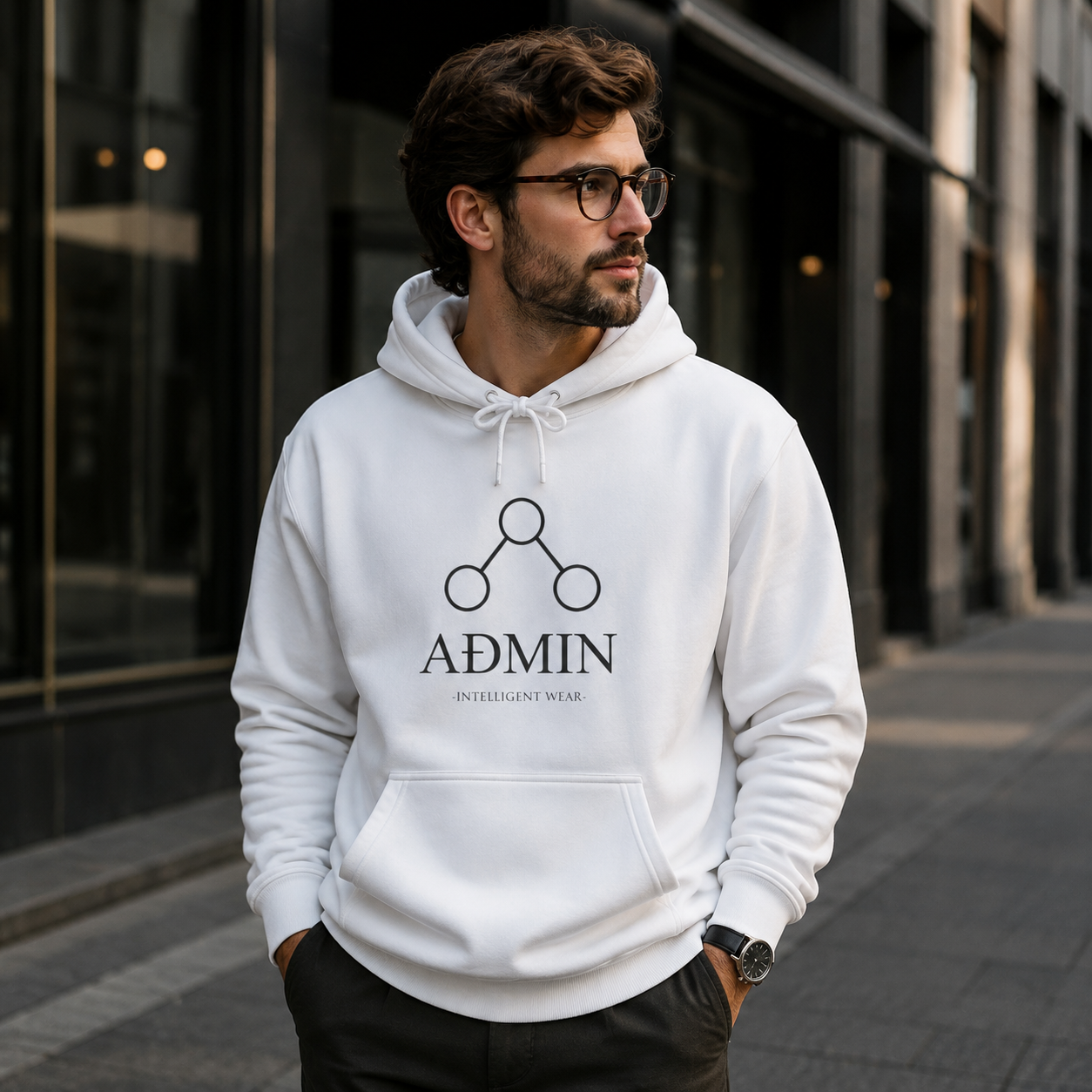 A man wearing a white pullover hoodie with a black graphic logo that reads 'ADMIN' and 'INTELLIGENT WEAR' stands on a city sidewalk in front of a modern glass building.