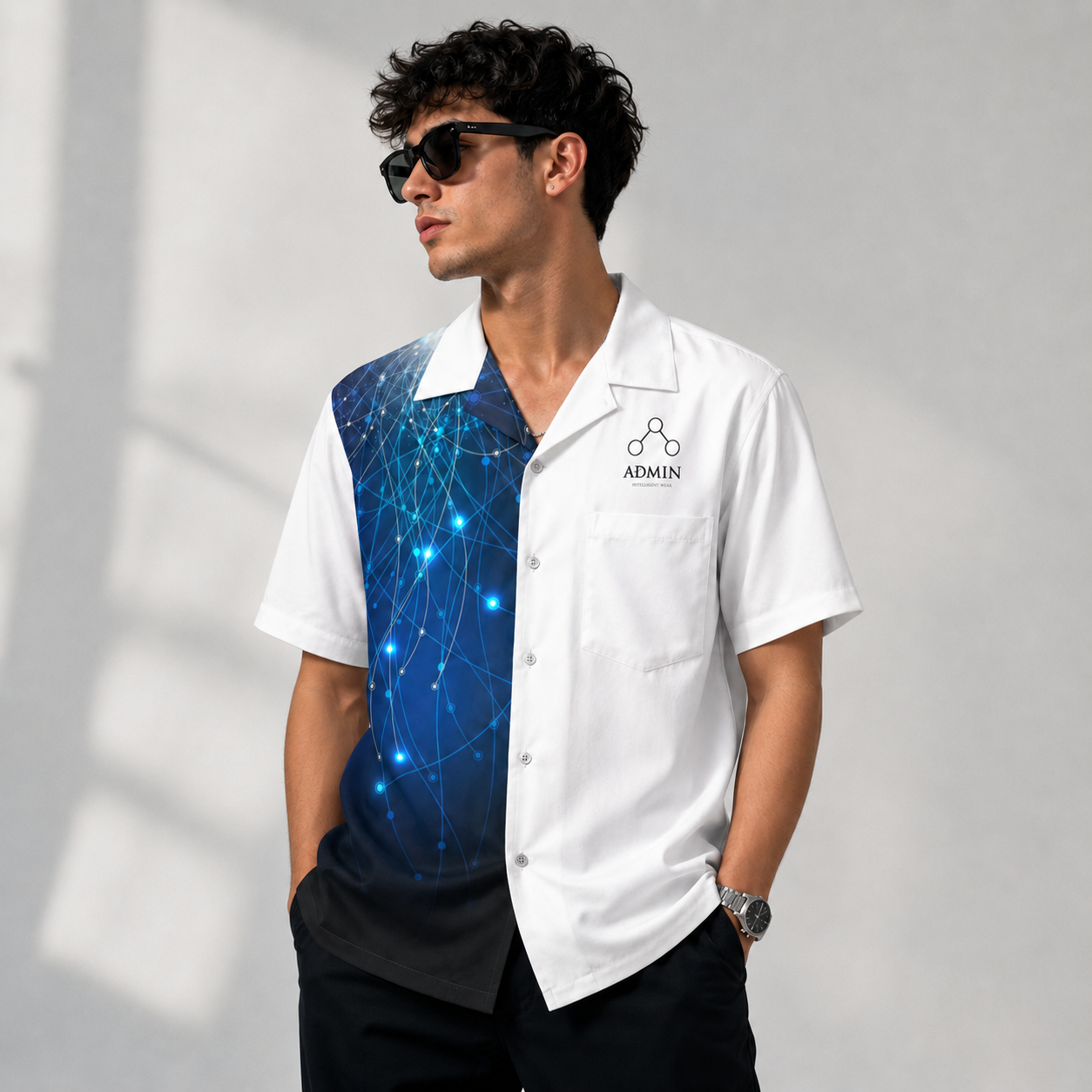 A man wearing a white short-sleeve button-up shirt with a blue network-pattern graphic panel on the chest, styled with black pants, sunglasses, and a watch against a light gray background.