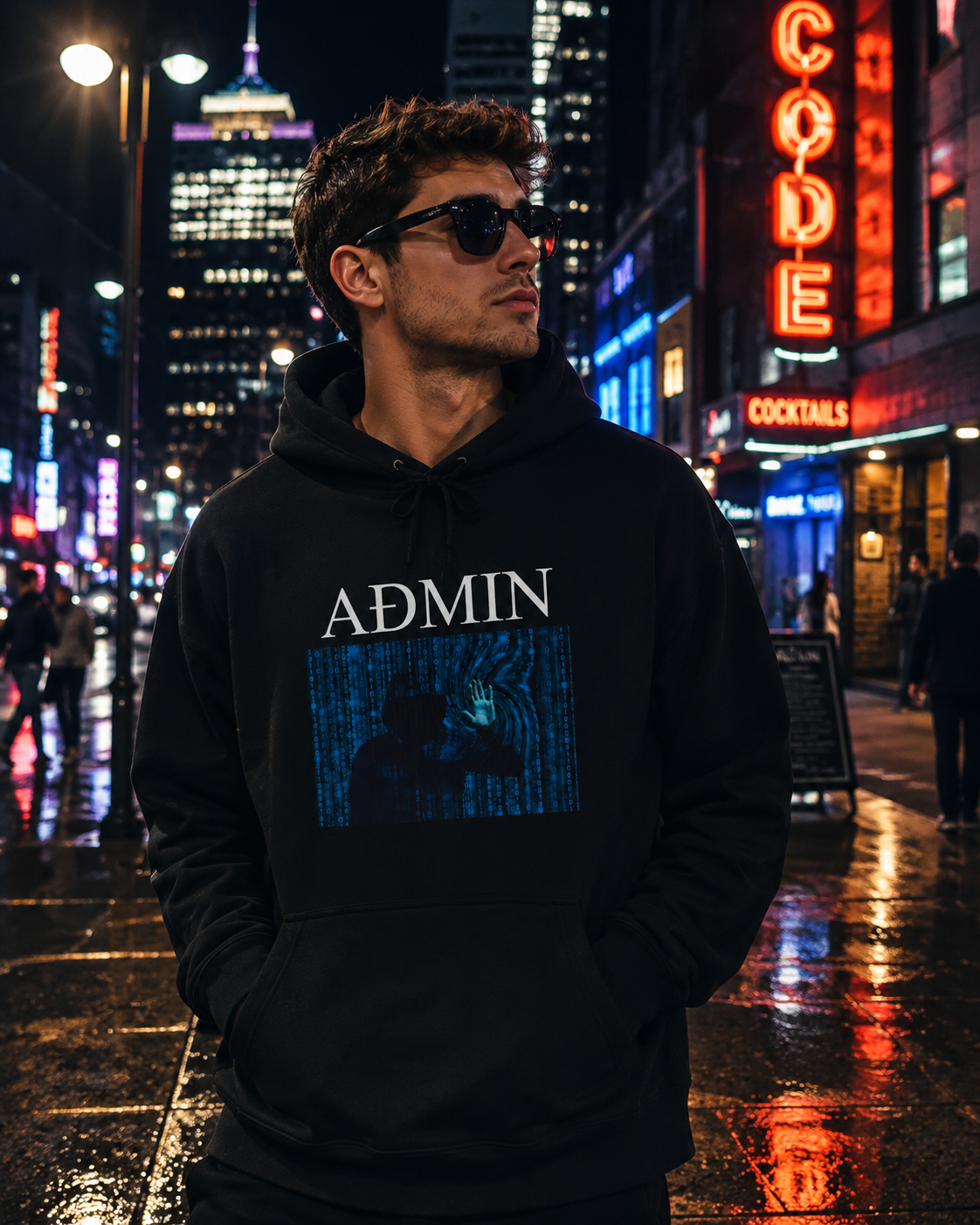 A man wearing a black hoodie with a blue digital matrix-style graphic and the word 'ADMIN' printed on the front, standing on a wet city street at night with neon signs in the background.