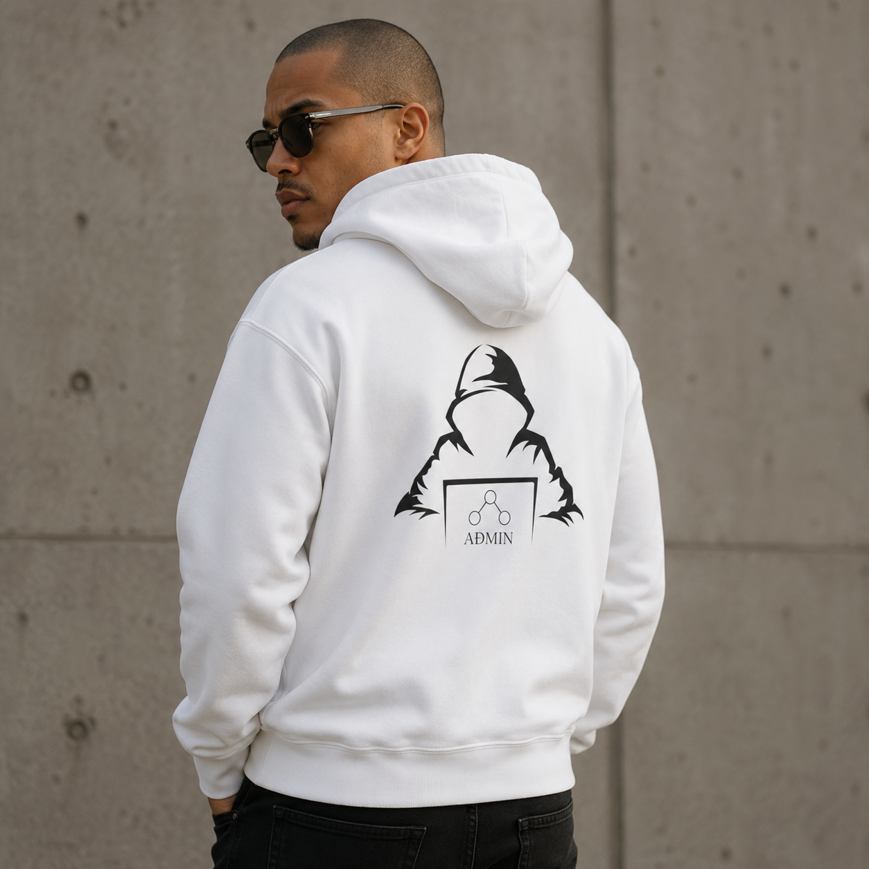 A man wearing a white hoodie with a black graphic print on the back, photographed from behind against a concrete wall.